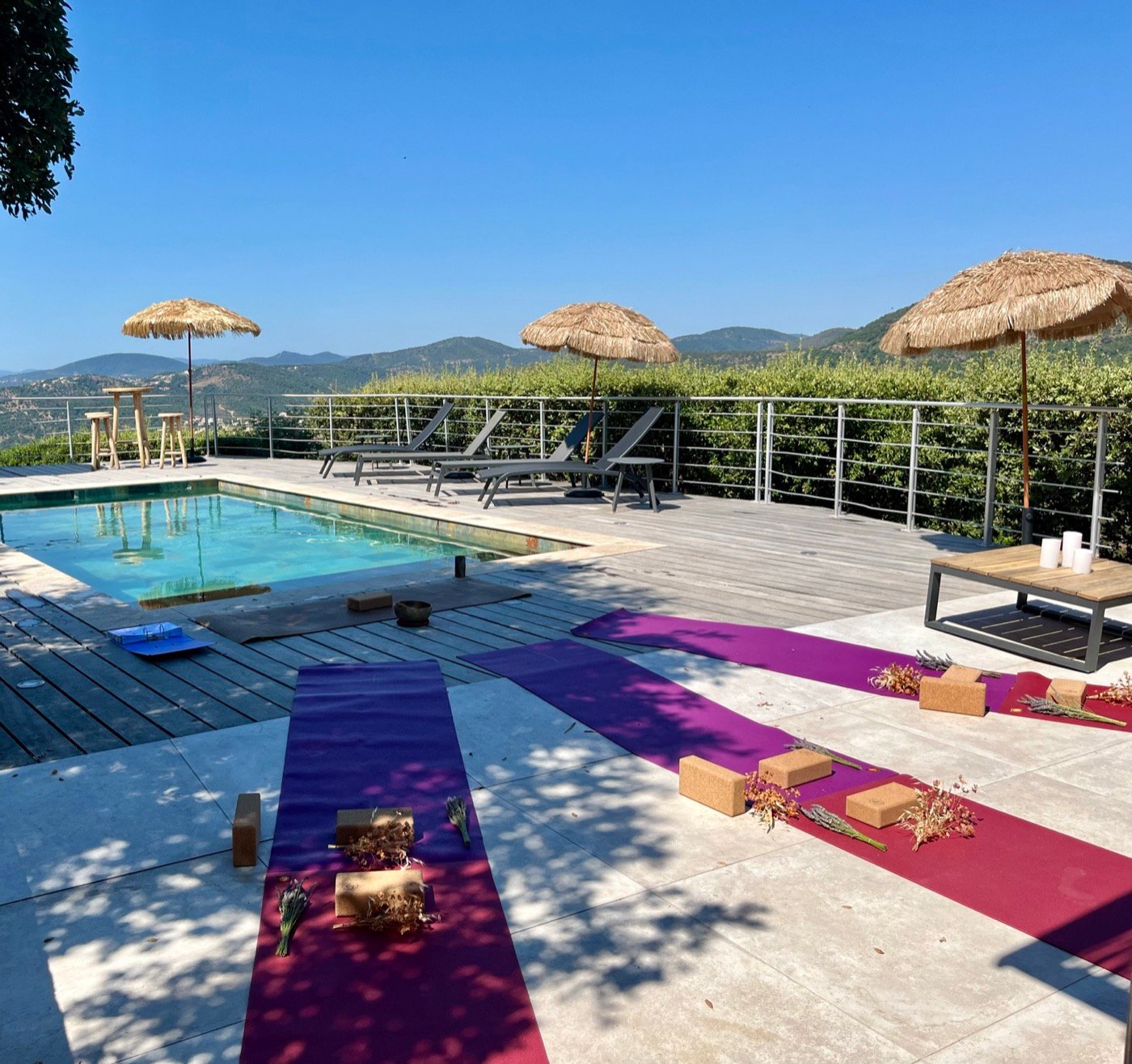 Tapis de yoga déroulés au bord d'une piscine, face aux collines, sous des parasols de paille